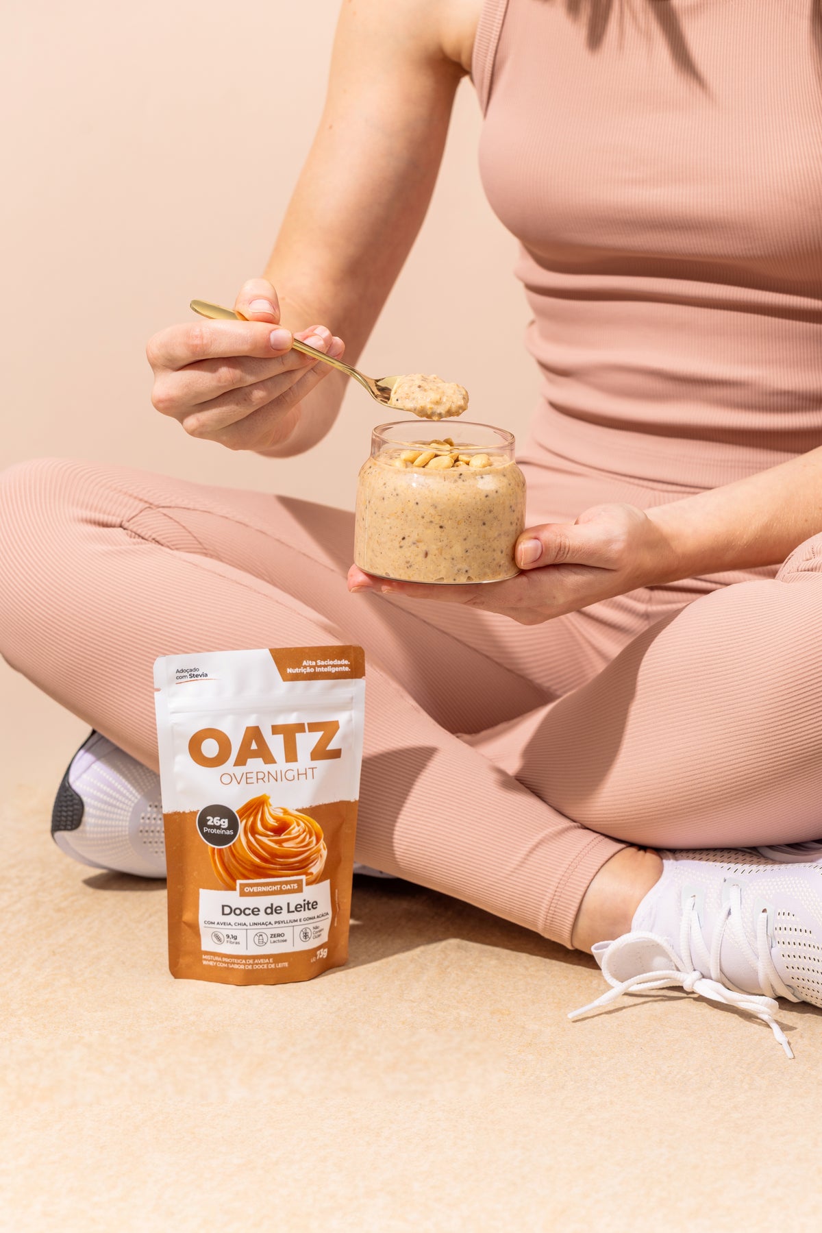 Mulher em roupa de treino comendo Oatz preparado, com o sachê de Doce de Leite ao lado